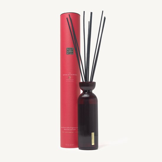 Rode kartonnen verpakking voor 'The Ritual of Ayurveda' geurstokjes, naast een gevulde donkere glazen diffuser.