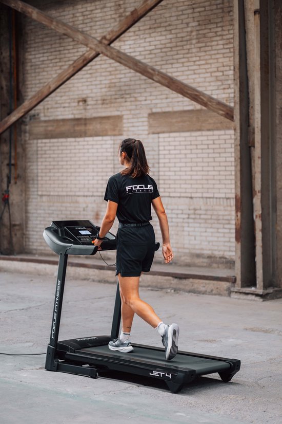 Vrouw loopt op zwarte Focus Fitness Jet 4 loopband, profiel van achteren.