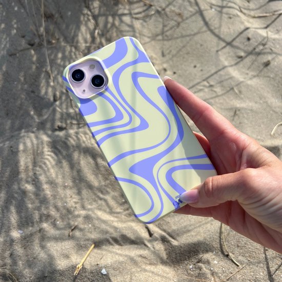 Hand houdt iPhone hoesje met geel en paars golvend patroon vast, op zand.
