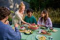 Mensen genieten van een buitenmaaltijd, een vrouw serveert een salade.