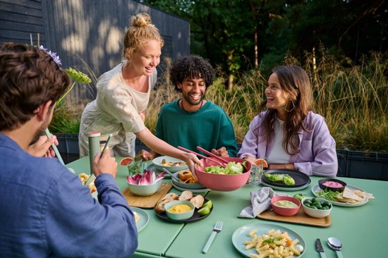 Mensen genieten van een buitenmaaltijd, een vrouw serveert een salade.