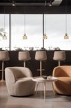 Twee lage fauteuils, één in beige en één in curry, bij een rond wit tafeltje in een woonkamer.