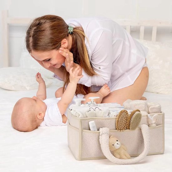 Moeder speelt met baby op bed naast een beige commandomand gevuld met babyartikelen.