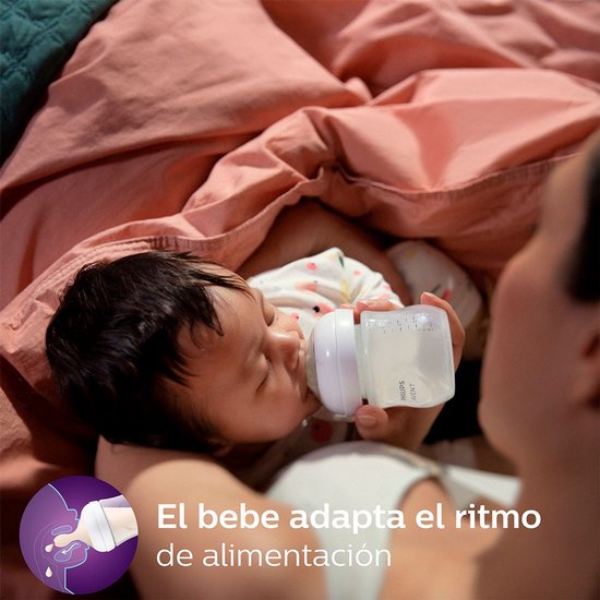 Een baby drinkt uit een Philips Avent fles, liggend op een roze deken. De tekst luidt 'El bebe adapta el ritmo de alimentación'.