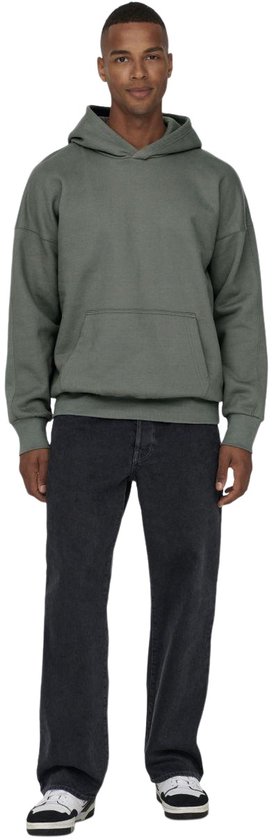 Een man draagt een oversized grijze hoodie en zwarte jeans, frontaal.