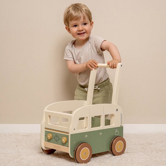 Lachend jongetje duwt een groene en beige houten loopwagen met ronde wielen.