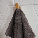 Une serviette brun foncé avec des détails côtelés suspendue à un crochet en bois.