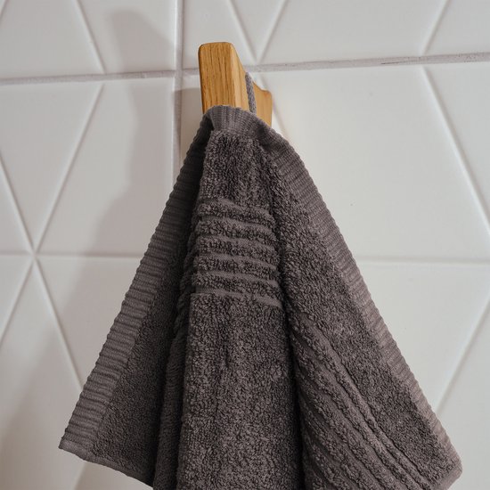Une serviette brun foncé avec des détails côtelés suspendue à un crochet en bois.