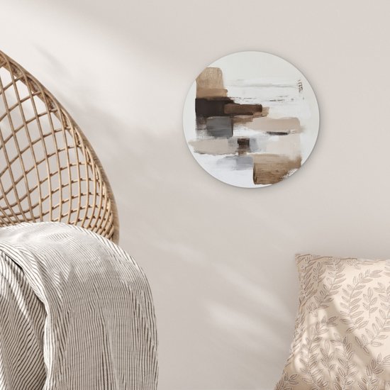 Ronde muurdecoratie met bruine en beige penseelstreken, hangend aan een muur boven een stoel.