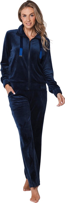 Een vrouw met haar hand in de zak van een donkerblauw velours huispak met rits. De set bestaat uit een vest en een lange broek.