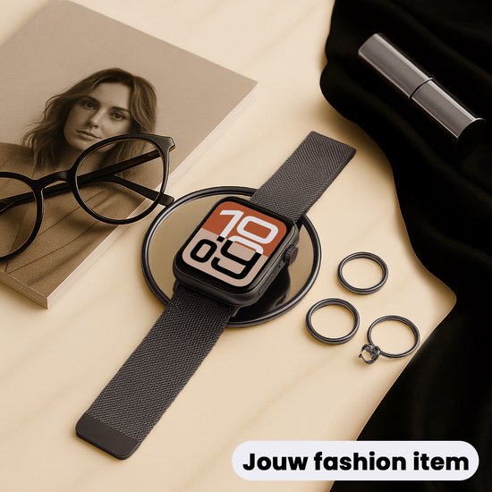 Zwart Milanese Apple Watch bandje op een spiegel, naast een bril en ringen, als modeaccessoire.