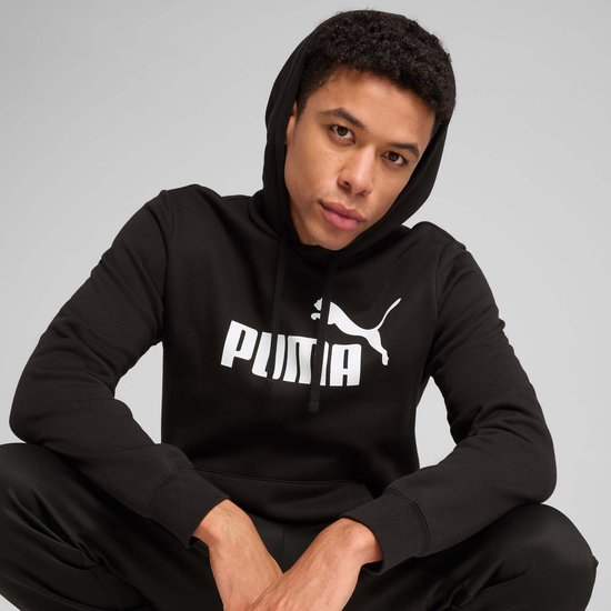 Close-up van een man die een zwarte PUMA hoodie draagt met een wit PUMA logo.