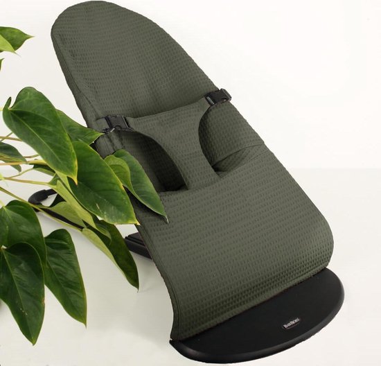 Groen wafelstof wipstoeltje met zwarte basis, naast een plant op witte achtergrond.