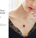 Een model draagt een gouden ketting met een rode hartvormige hanger met vleugels.
