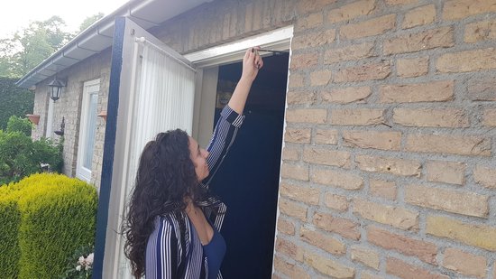 Een vrouw met krullend haar en gestreept shirt reikt naar de bovenkant van een deuropening.