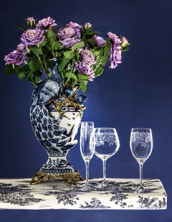 Un vase à motif de paon avec des fleurs violettes, à côté d'un verre à champagne, d'un verre à vin et d'un verre à martini.