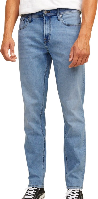 Man met een witte t-shirt en blauwe jeans. De focus ligt op de jeans met knopen.