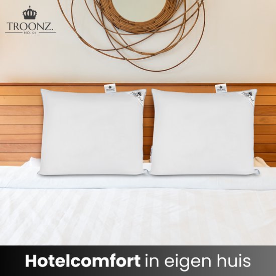 Twee witte Troonz kussens met logo op een gestreept hotelbed. Hotelcomfort in eigen huis.