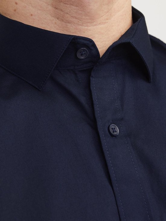 Man met marineblauw overhemd en beige broek, staand, achterkant.
