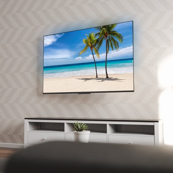 Un grand téléviseur à écran plat affichant un paysage de plage, monté sur un mur au-dessus d'un meuble TV blanc.