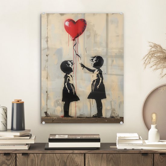 Street art-glasafbeelding van twee silhouetkinderen die naar een rode ballon in hartvorm reiken, bevestigd aan de muur.