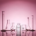 Een fles Olaplex Hair Perfector No.3 staat tussen laboratoriumglaswerk tegen een roze achtergrond.