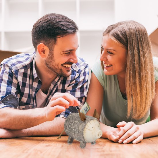 Een koppel lacht naar elkaar terwijl de man geld in een spaarvarken met schors-look plaatst.