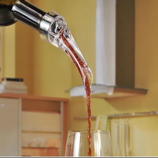 Rode wijn wordt uit een fles door een transparante schenker in een wijnglas gegoten.