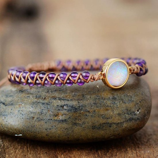Gevlochten armband met paarse amethist kralen en een ronde, witte Marly Quartz steen, liggend op een steen.