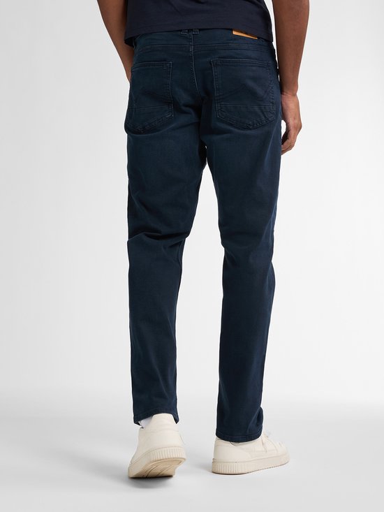 Man met de rug naar de camera, draagt een donkerblauwe jeans.