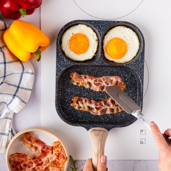 Poêle antiadhésive grise aspect marbre, avec des œufs au plat et du bacon, à côté de poivrons jaunes et rouges.