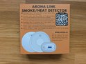 Doos van Aroha Link rook/hitte detector met QR-code, afbeeldingen van detectors en meertalige productinformatie.