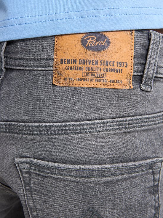 Close-up van de bruine leren Petrol Industries patch op de achterkant van een grijze jeans.