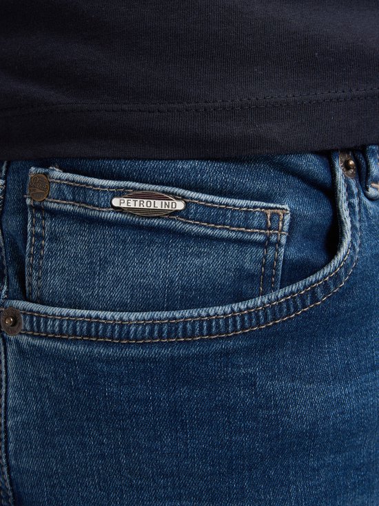 Detail van de voorzak van een blauwe spijkerbroek met metalen 'Petrol Ind.' plaatje.