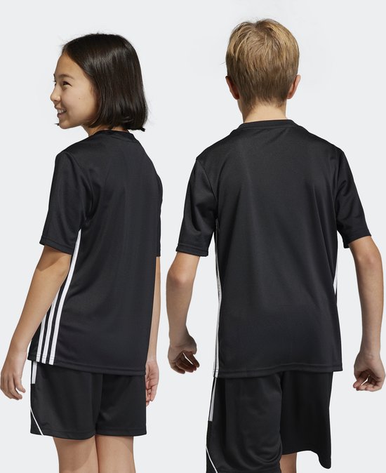 Kinderen in zwarte Tabela 23 voetbalshirts met witte Adidas-strepen op de mouwen en zijkanten.