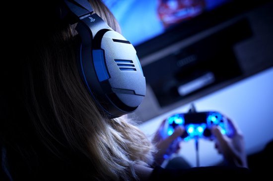 Persoon met blonde haren draagt een zwarte en blauwe gaming headset en speelt op een PlayStation.