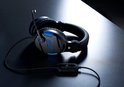 Zwarte en blauwe stereo gaming headset met microfoon en volumeregelaar op een donkere tafel.