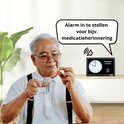 Oudere man neemt medicatie bij een OER dementieklok. Tekst in spraakballon: 'Alarm in te stellen voor bijv. medicatieherinnering'.