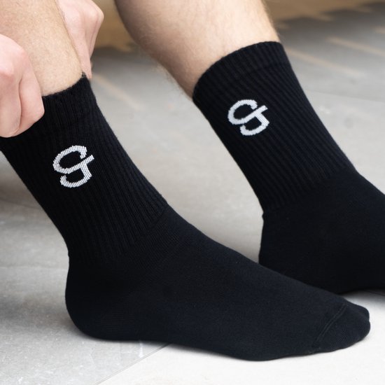 Zwarte sok met wit logo 'G'. Getoond op een persoon die de sok aantrekt.