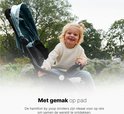 Een kind zit lachend in een lichtgroene buggy in een park.