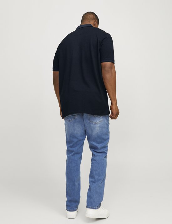 Man van achteren in donkerblauw poloshirt, blauwe jeans en witte sneakers.