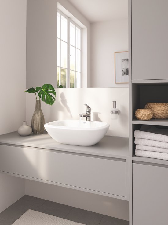 Badkamer met ovale wasbak, chromen kraan en zeepdispenser.