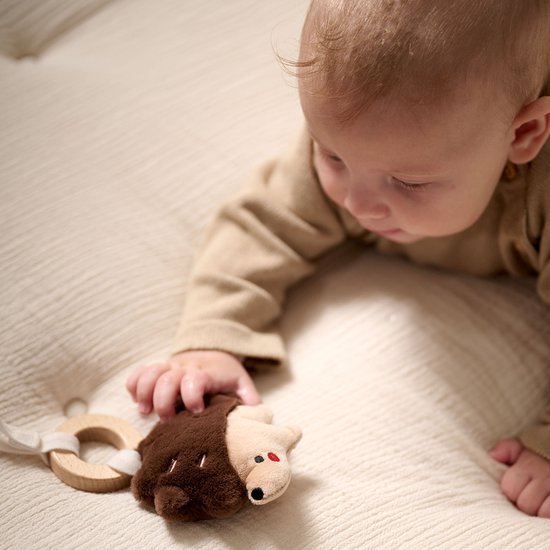 Baby met bruine knuffel egel met rode oogjes en snuit.