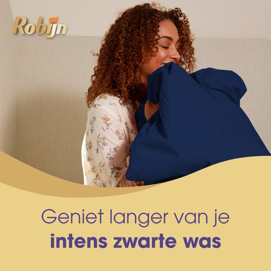 Vrouw met krullend haar, genietend van donkerblauw beddengoed. Tekst: Geniet langer van je intens zwarte was.