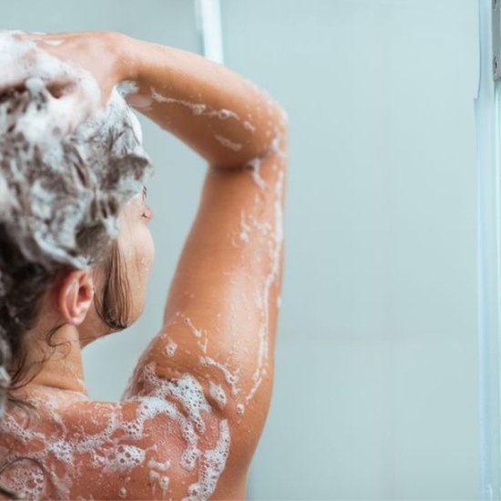 Femme aux cheveux bouclés sous la douche, se lavant les cheveux avec du shampooing moussant.