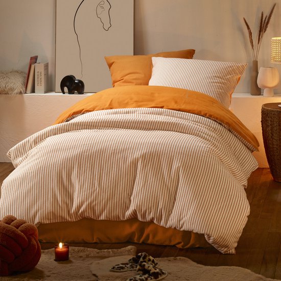 Un lit fait avec de la literie orange et rayée, des oreillers et une couverture.