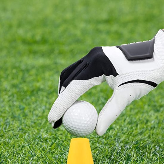 Hand met een witte en zwarte golfhandschoen plaatst een golfbal op een gele golf tee op groen gras.