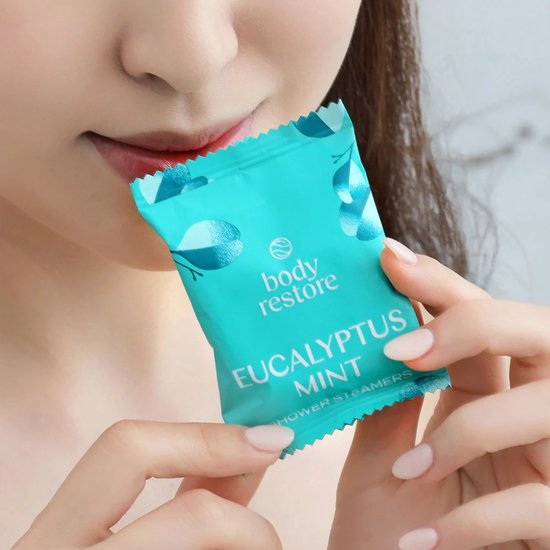 Een vrouw houdt een turquoise verpakte Body Restore Eucalyptus Mint douchetablet dicht bij haar gezicht.