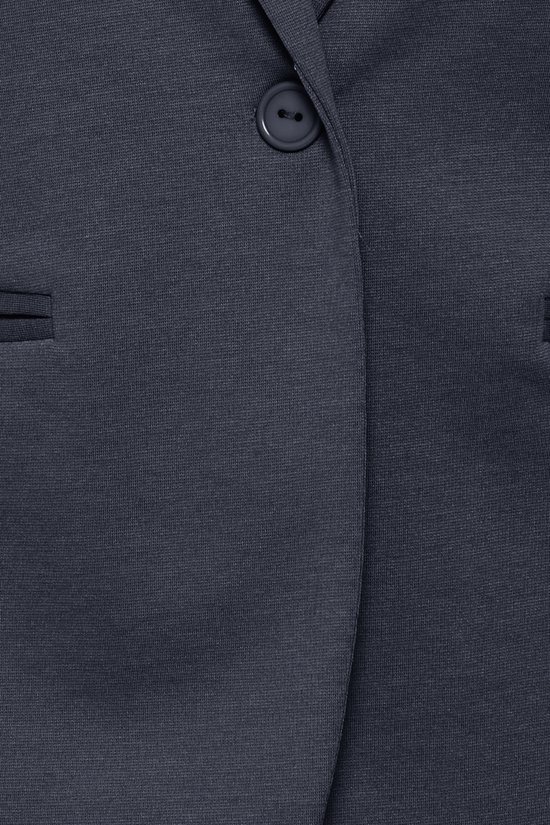 Detailopname van een marineblauwe blazer met een knoop en opgestikte zakken.
