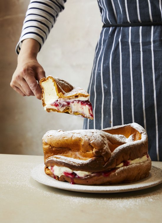 Een pannenkoek met slagroom en rode vruchten, bestrooid met poedersuiker. Een stuk wordt eruit gehaald.